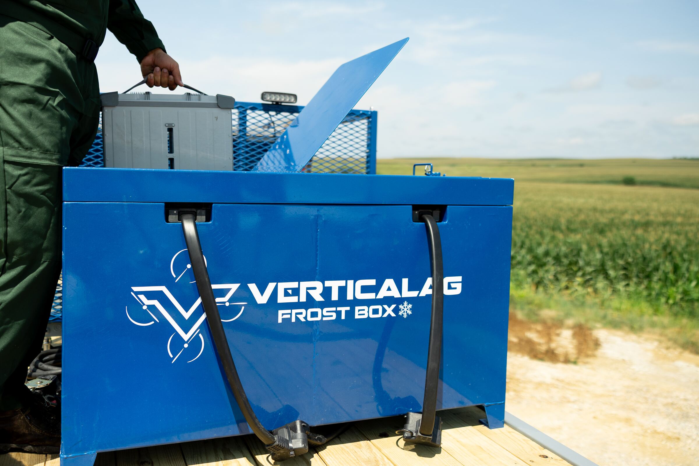 Operator loading a DJI Agras battery into the Frost Box on a trailer beside a cornfield
